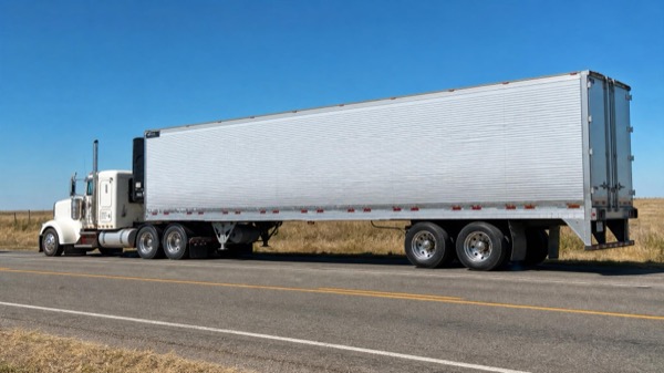 White refrigerated trailer prominent on a sun-baked interstate under clear summer sky