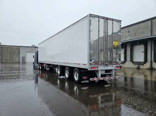 Vanguard reefer trailer backed into an industrial loading dock on a heavy rainy day with wet reflective pavement