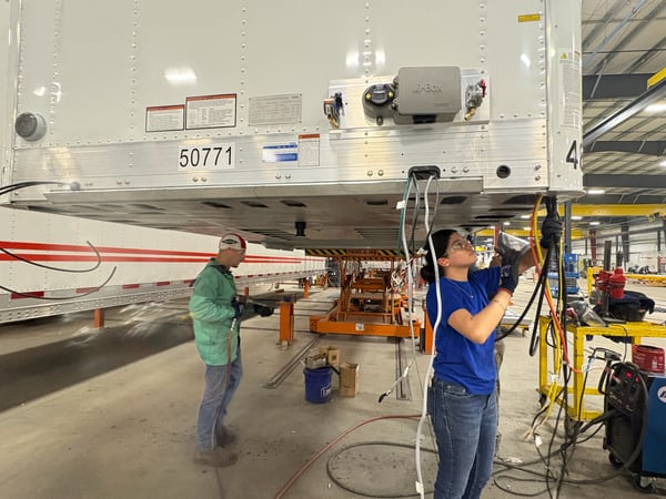 Two Vanguard workers routing electrical wiring beneath a reefer trailer