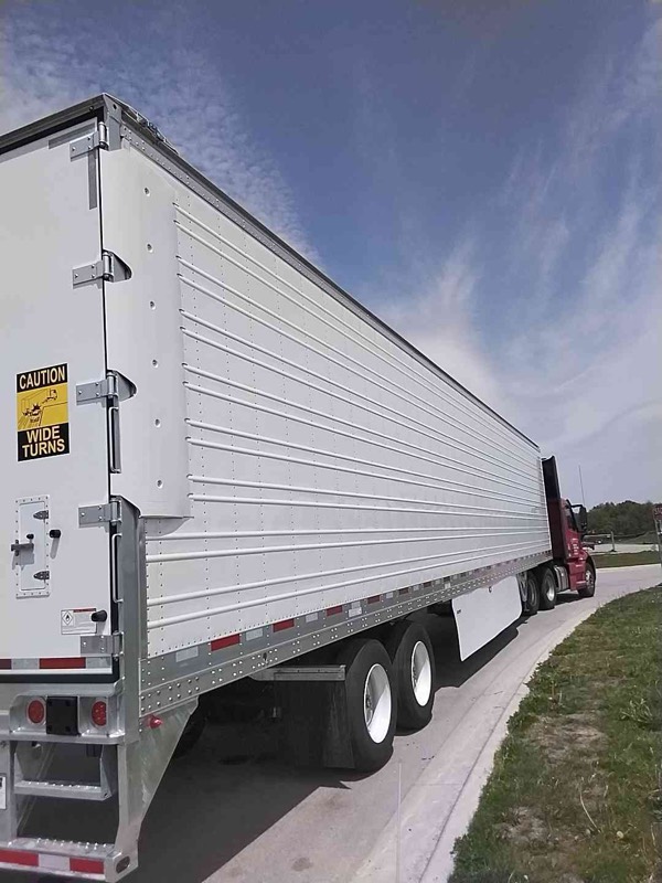 A clean white Vanguard reefer trailer hitched to a red day-cab tractor, parked curbside on a road under a blue sky