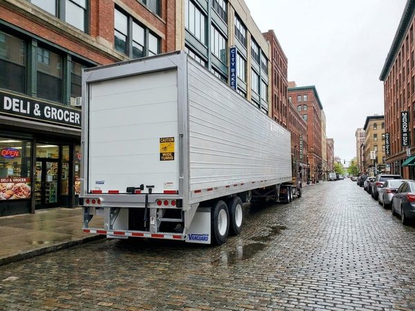 Vanguard reefer trailer parked on a wet cobblestone city street outside a deli and grocer on a delivery route